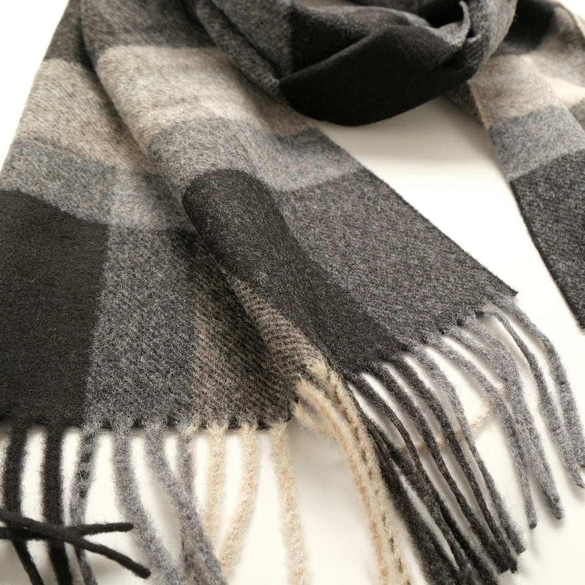 Close-up of charcoal plaid scarf with cream-and-gray checks and fringed hem