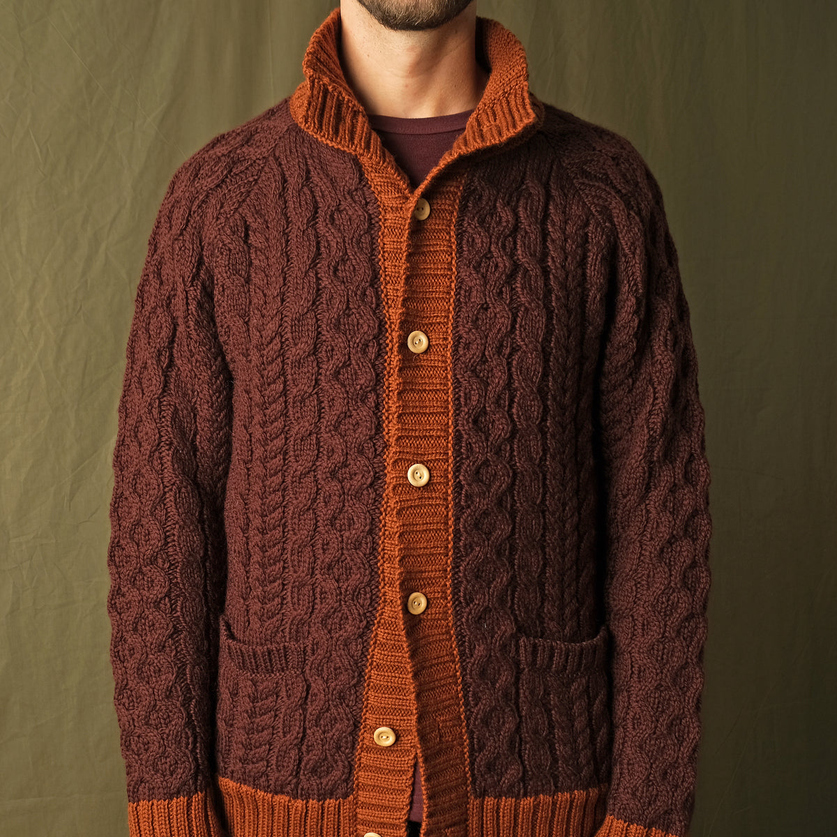 Dark maroon cable-knit mock neck cardigan with orange buttons, placket, and patch pockets