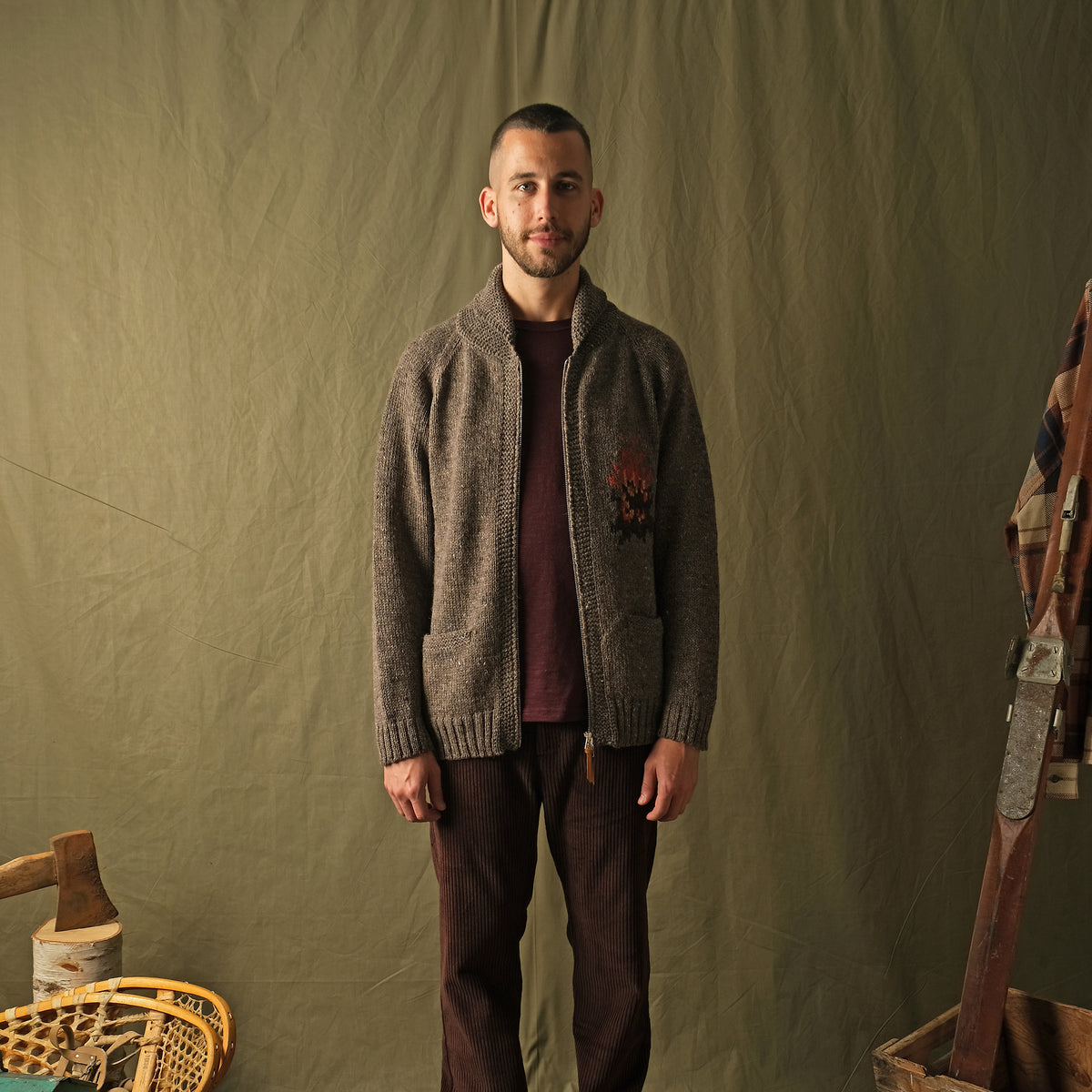 Brown zip cardigan worn by a man with left-chest campfire embroidery