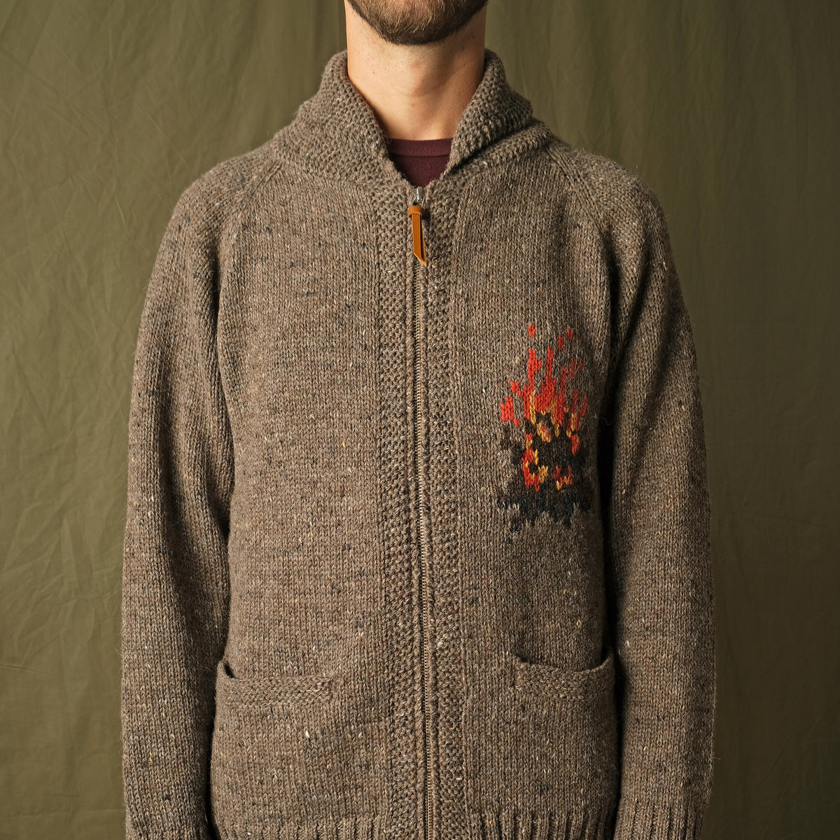 Brown full-zip cardigan worn by a man, campfire motif on the chest and ribbed hem