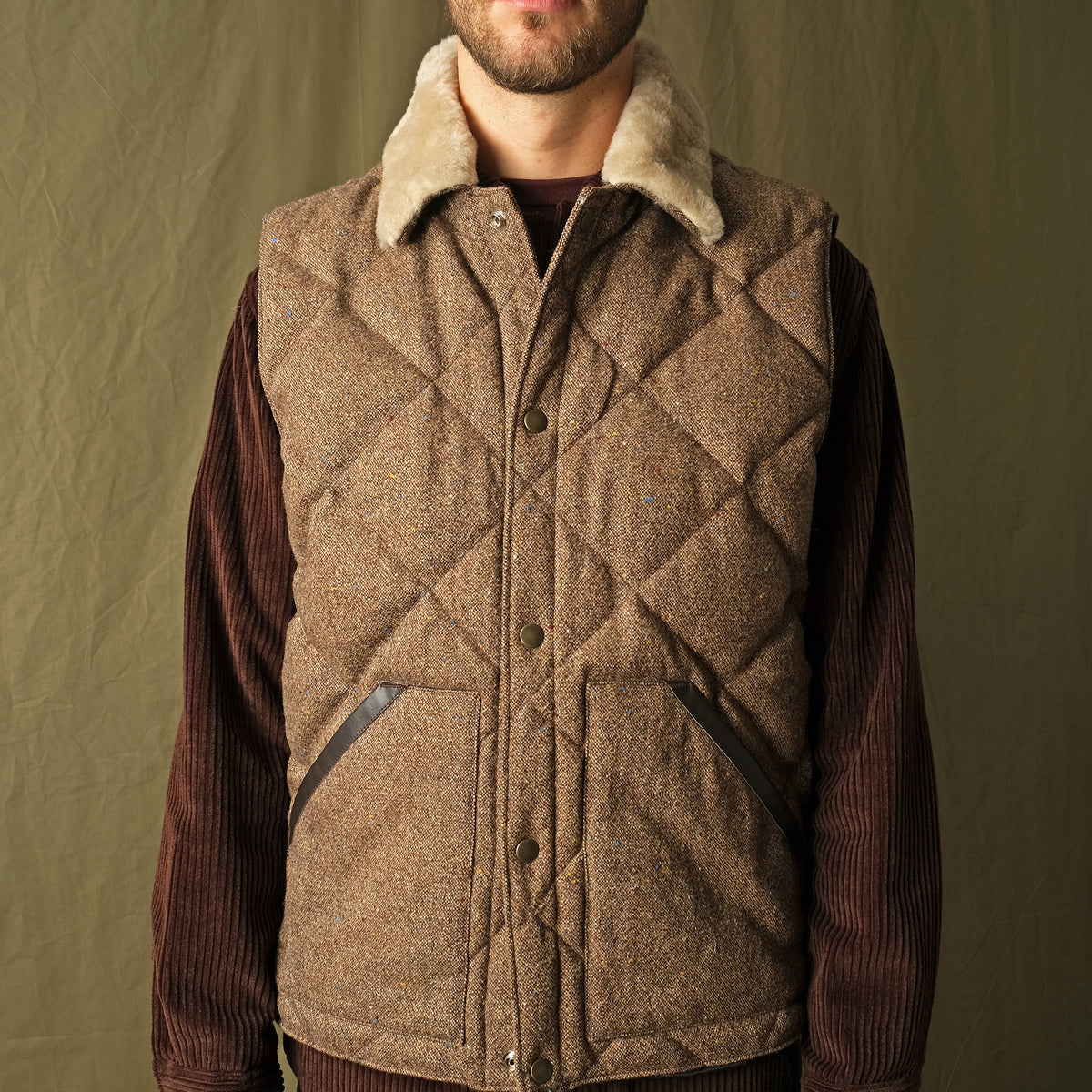 Brown diamond-quilted down vest with tan sherpa collar over ribbed knit sleeves