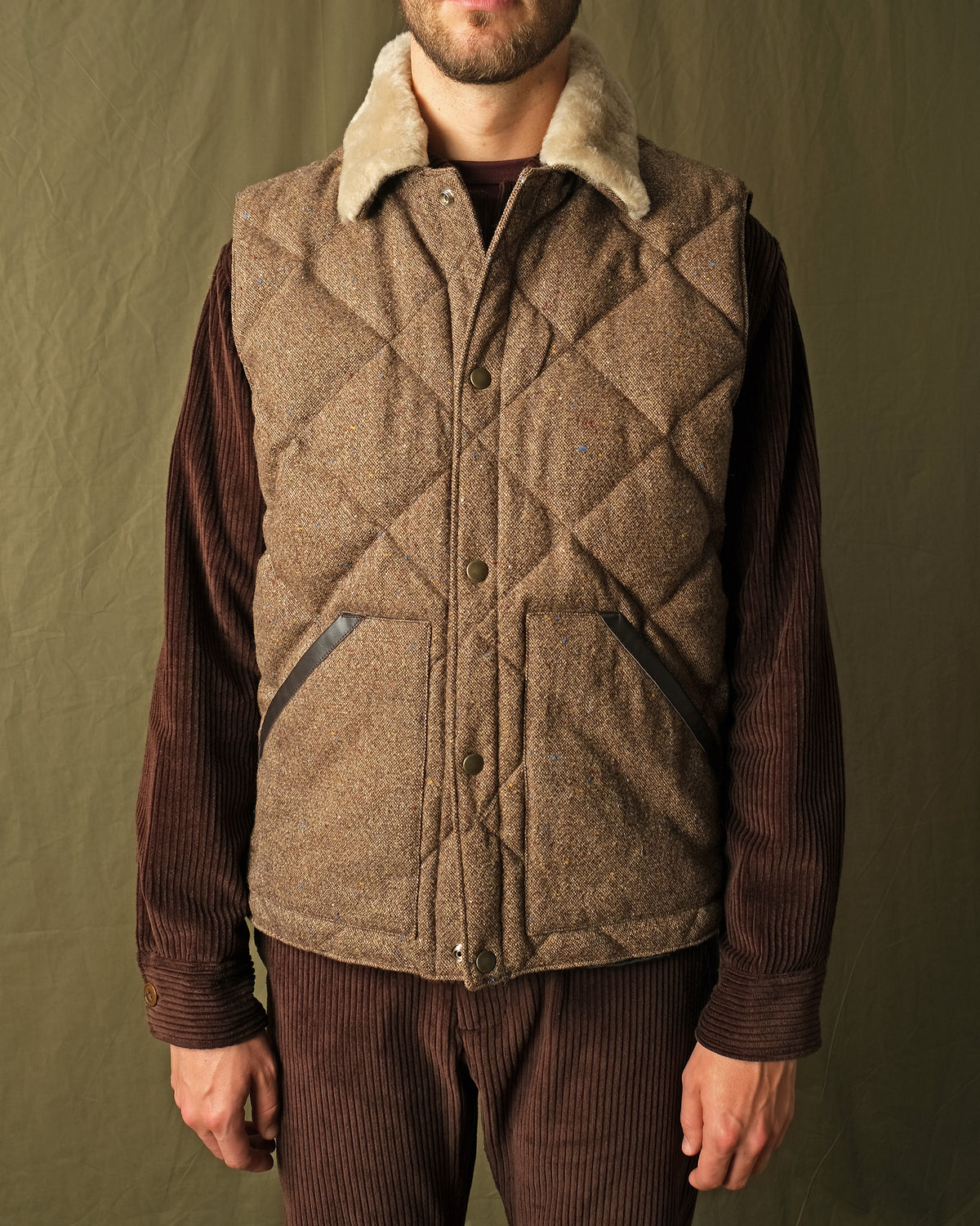 Brown diamond-quilted down vest with tan sherpa collar over ribbed knit sleeves