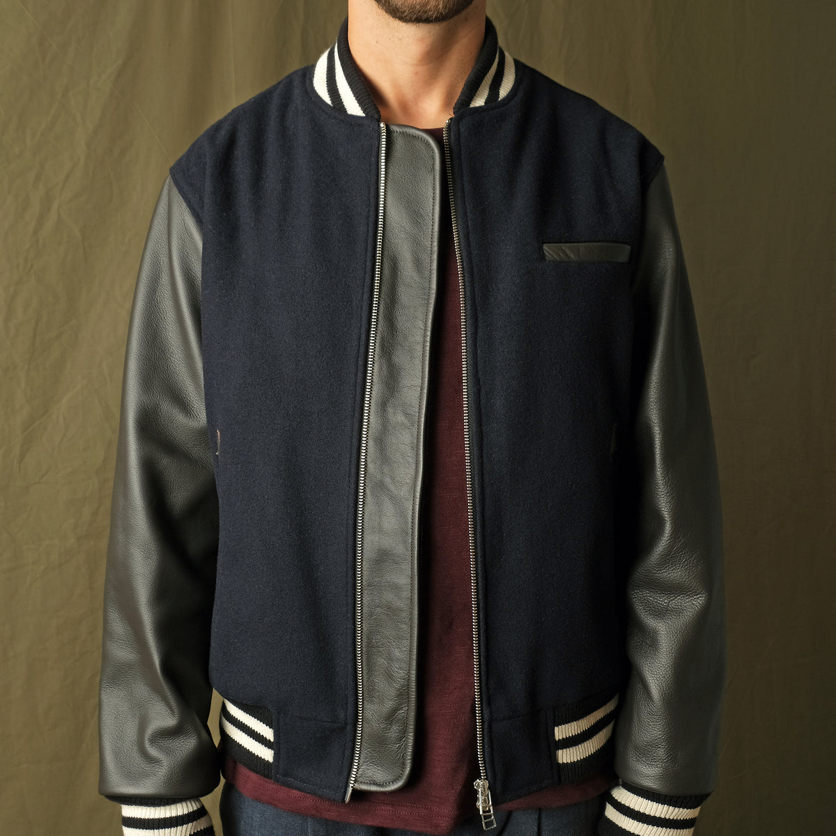 Navy bomber jacket with leather-look sleeves, striped cuffs, and front zipper