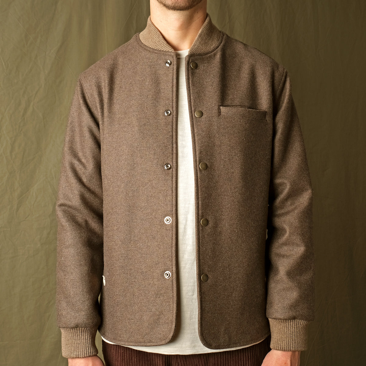 Brown stadium jacket close-up with snap buttons, stand collar, and chest pocket