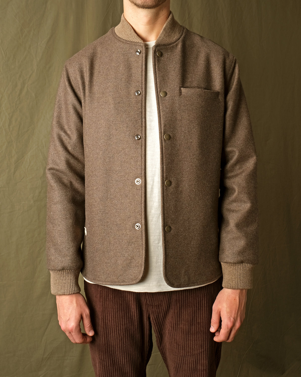 Brown stadium jacket close-up with snap buttons, stand collar, and chest pocket