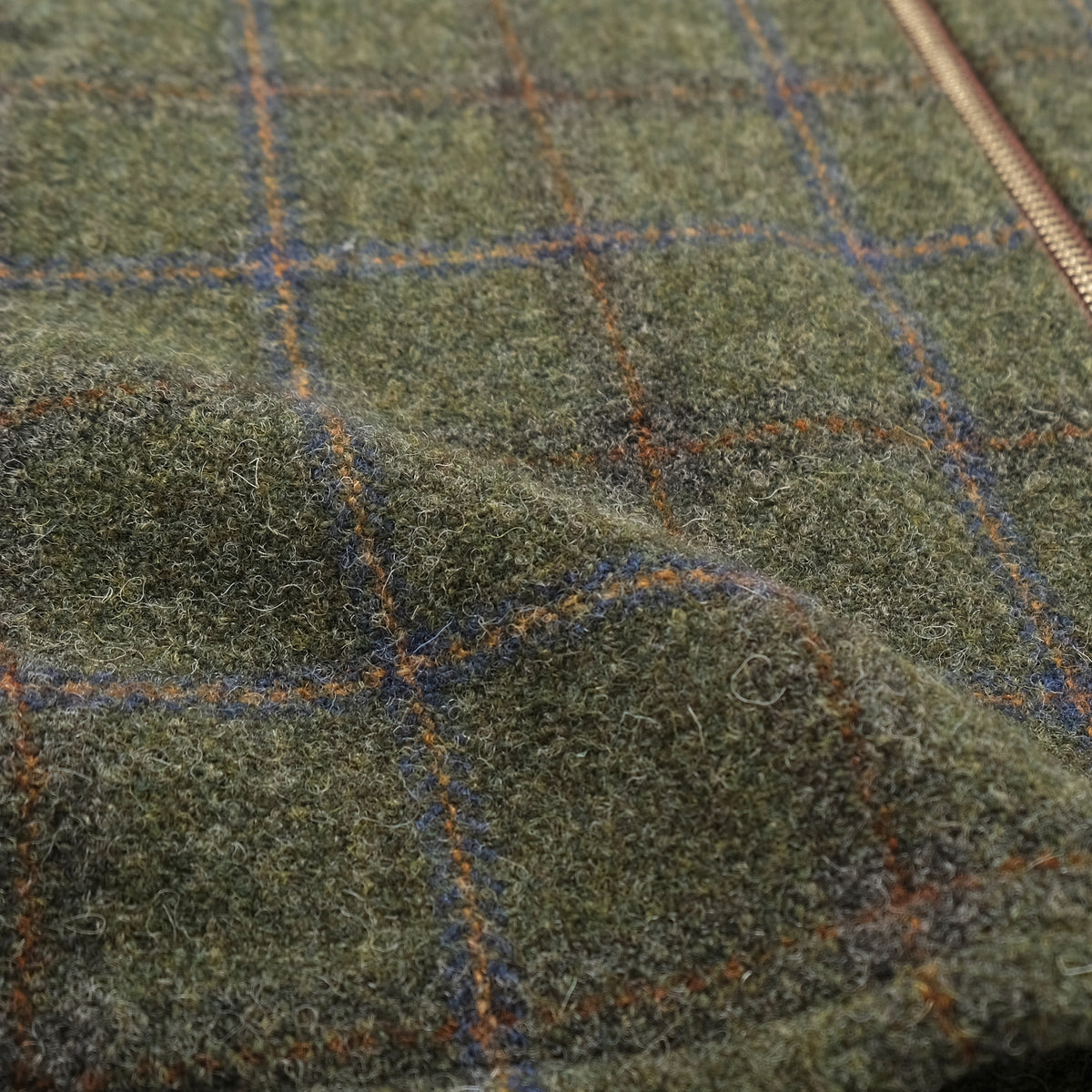 Olive green plaid wool fabric with textured weave and blue and orange grid lines