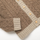 Cable knit cardigan showing cream button placket, ribbed hem, and side pocket