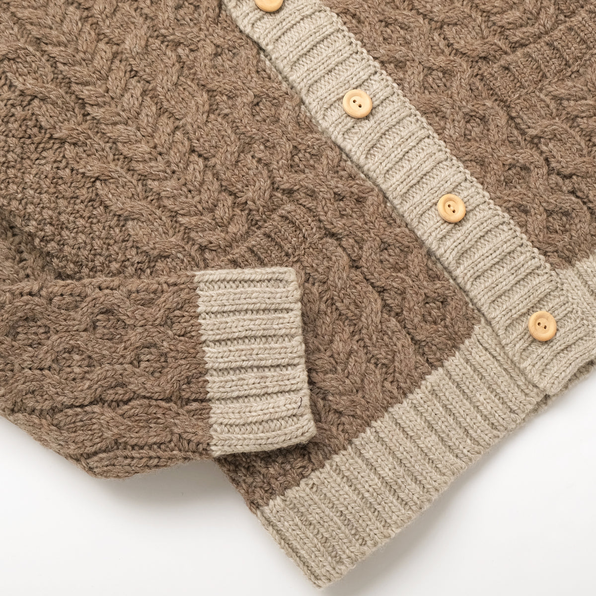Cable knit cardigan showing cream button placket, ribbed hem, and side pocket
