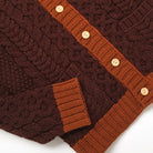 Dark maroon cable-knit cardigan with orange cuffs, textured knit, and pocket detail