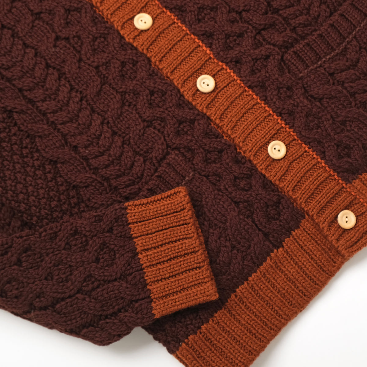 Dark maroon cable-knit cardigan with orange cuffs, textured knit, and pocket detail