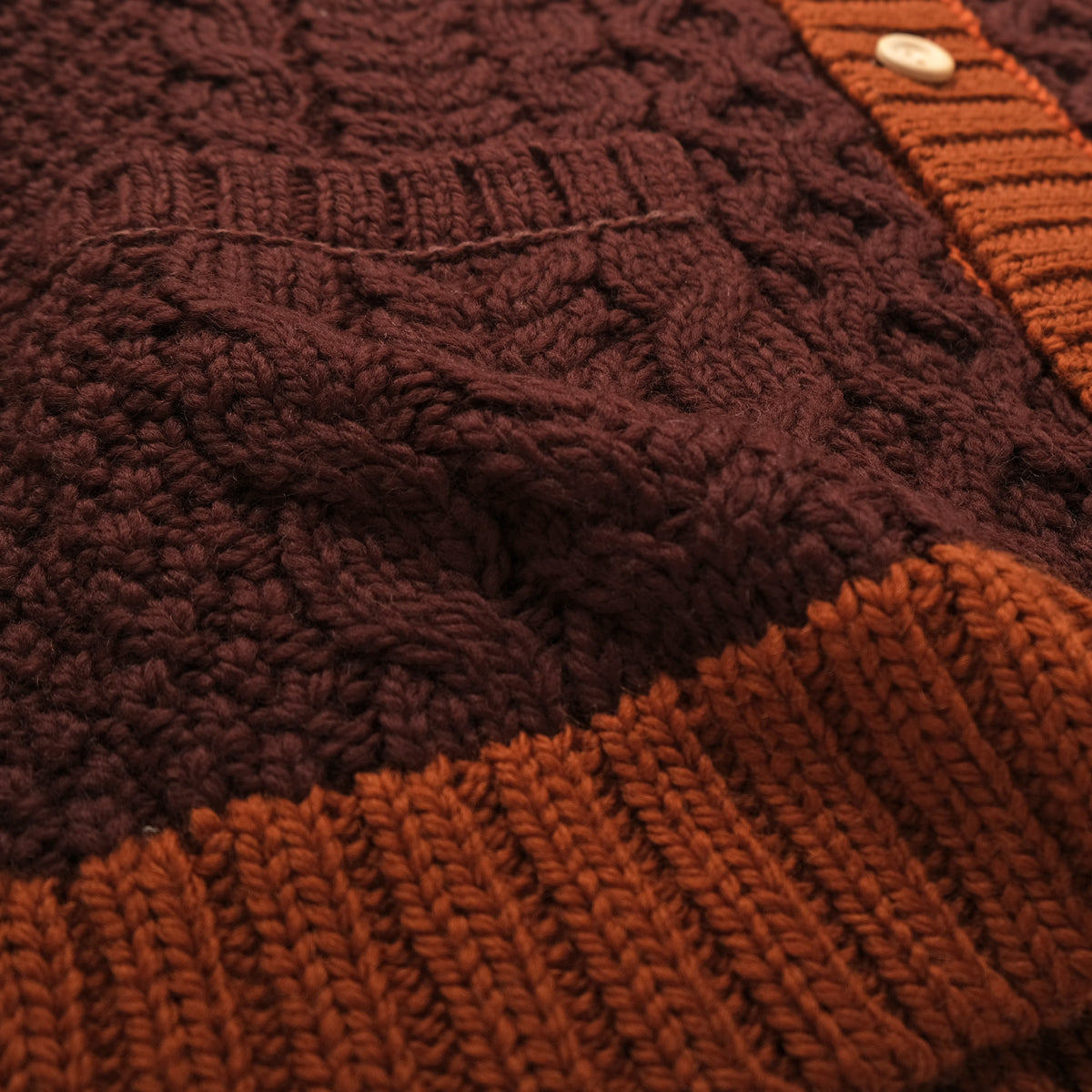 Cable-knit cardigan texture with orange ribbed trim at mock neck and hem
