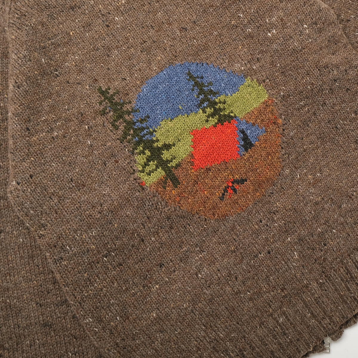 Brown knit fabric close-up of camp scene embroidery near the chest