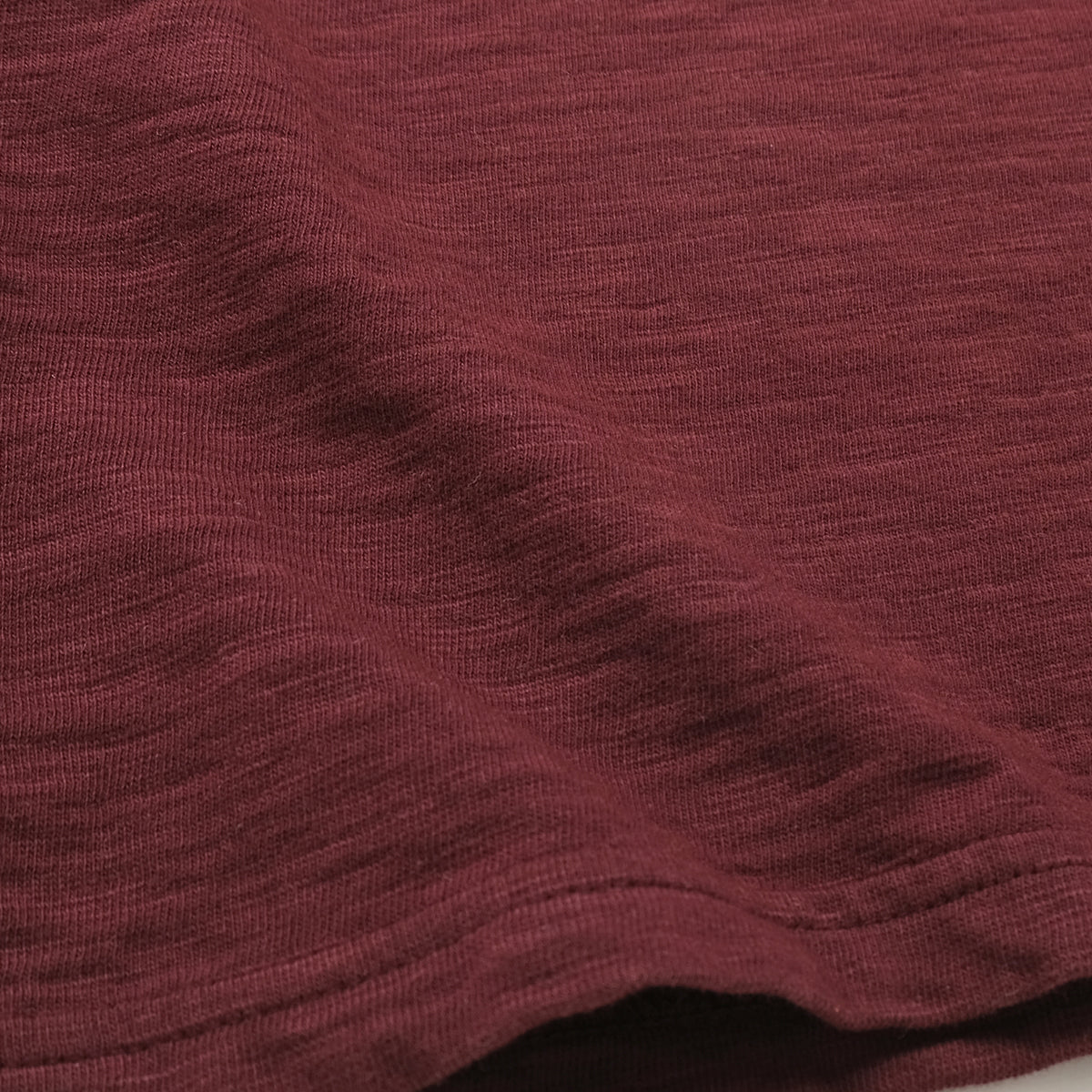 Maroon double slub long-sleeve T-shirt fabric close-up, textured weave.