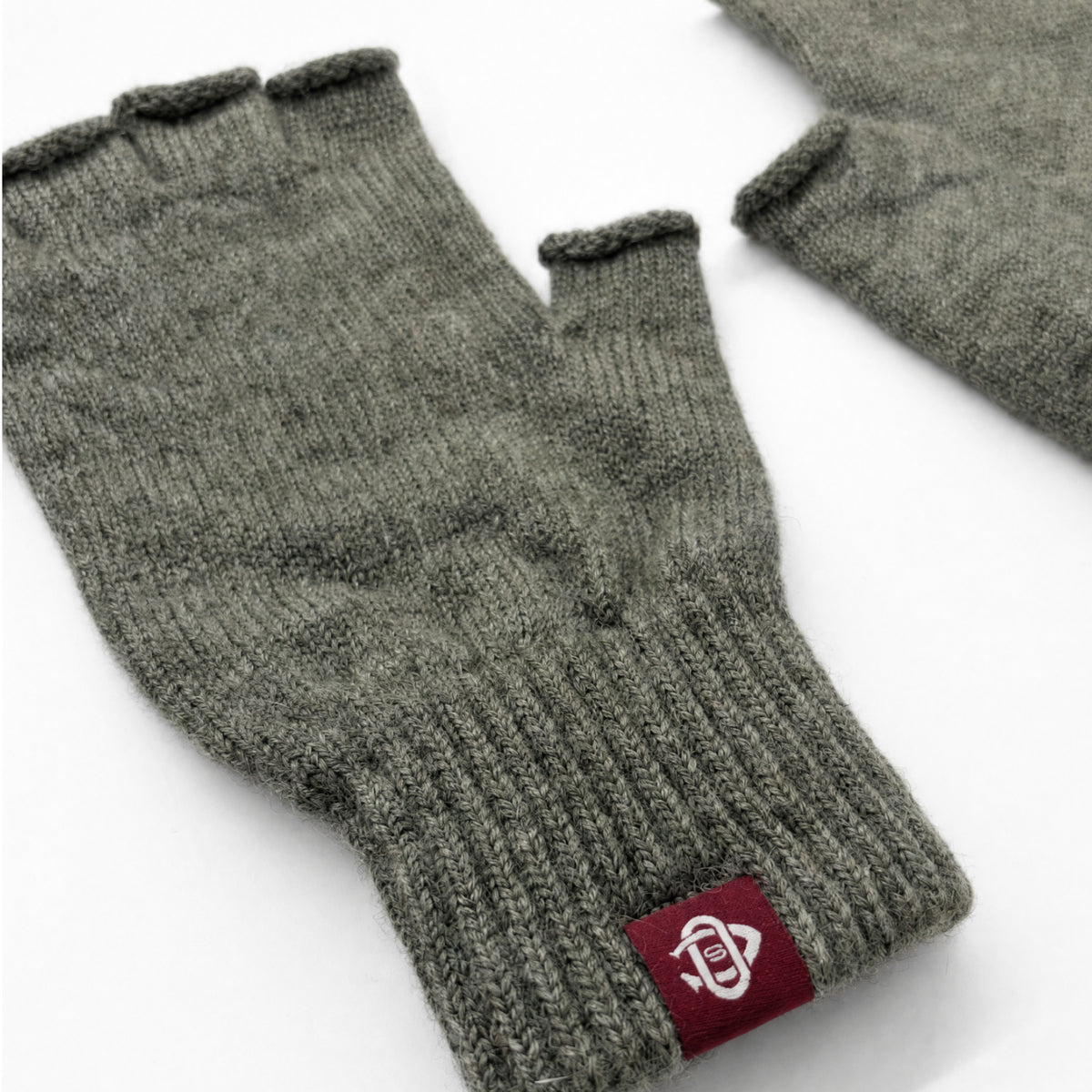 Dark green ribbed wool fingerless glove with red logo patch, close-up