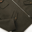 Olive wool field jacket detail with flap pocket, snap buttons, and zipper