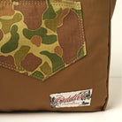 Reversible tote bag close-up of brown panel, camo pocket, and logo patch