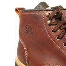 Brown hiking boot close-up with lace-up eyelets, dark tongue, stitched crest logo.