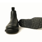 Black Chelsea boot outsole close-up, lugged tread and stacked heel profile