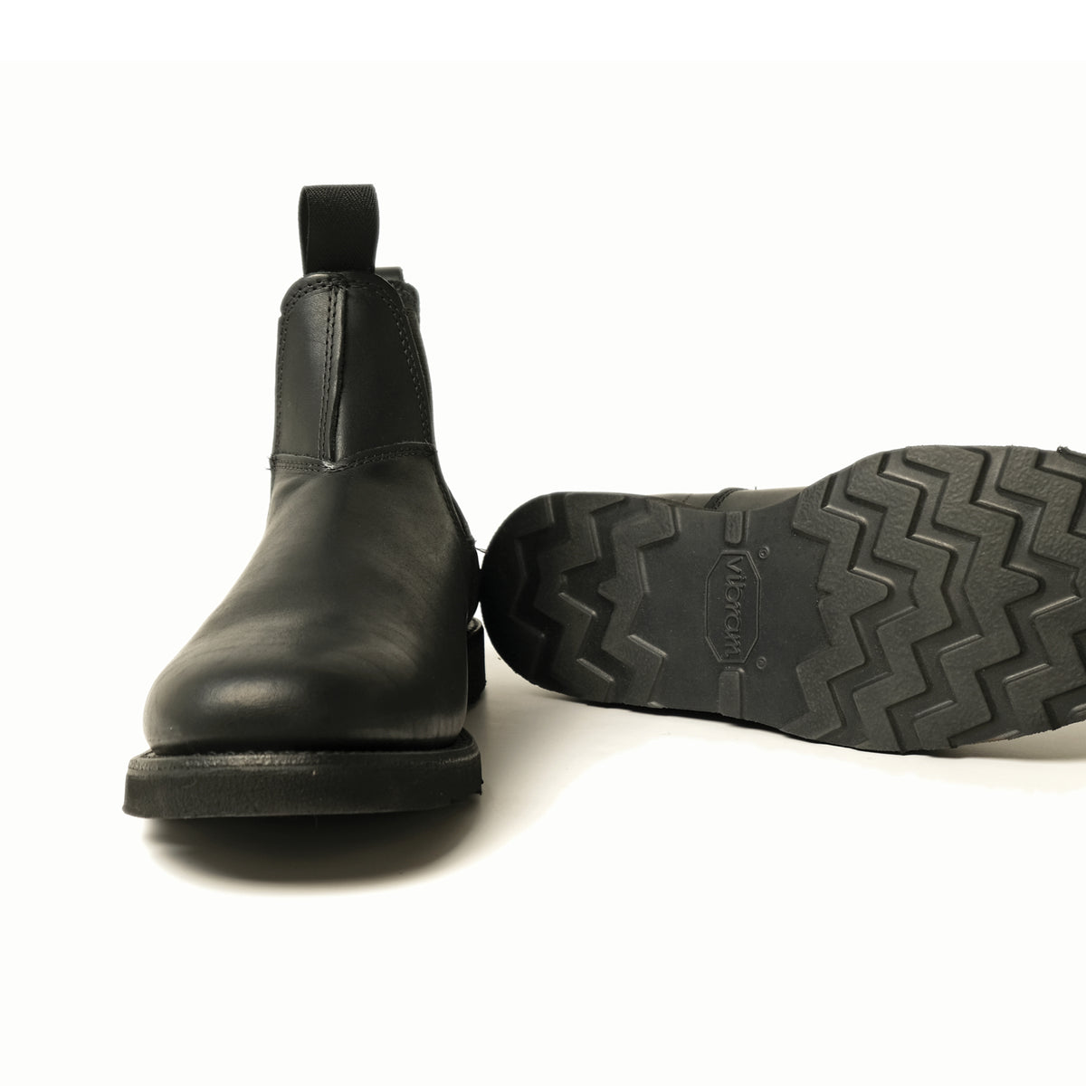 Black Chelsea boot outsole close-up, lugged tread and stacked heel profile