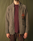 Brown full-zip cardigan worn by a man, showing left-chest campfire embroidery
