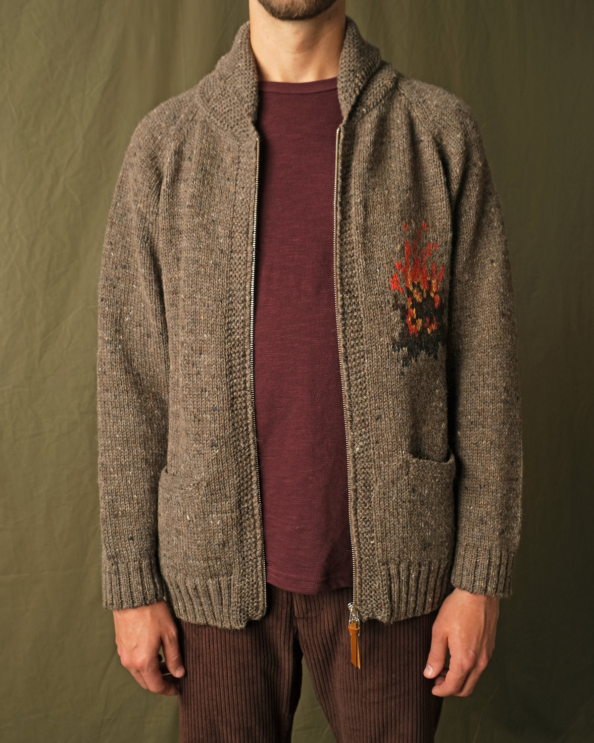 Brown full-zip cardigan worn by a man, showing left-chest campfire embroidery