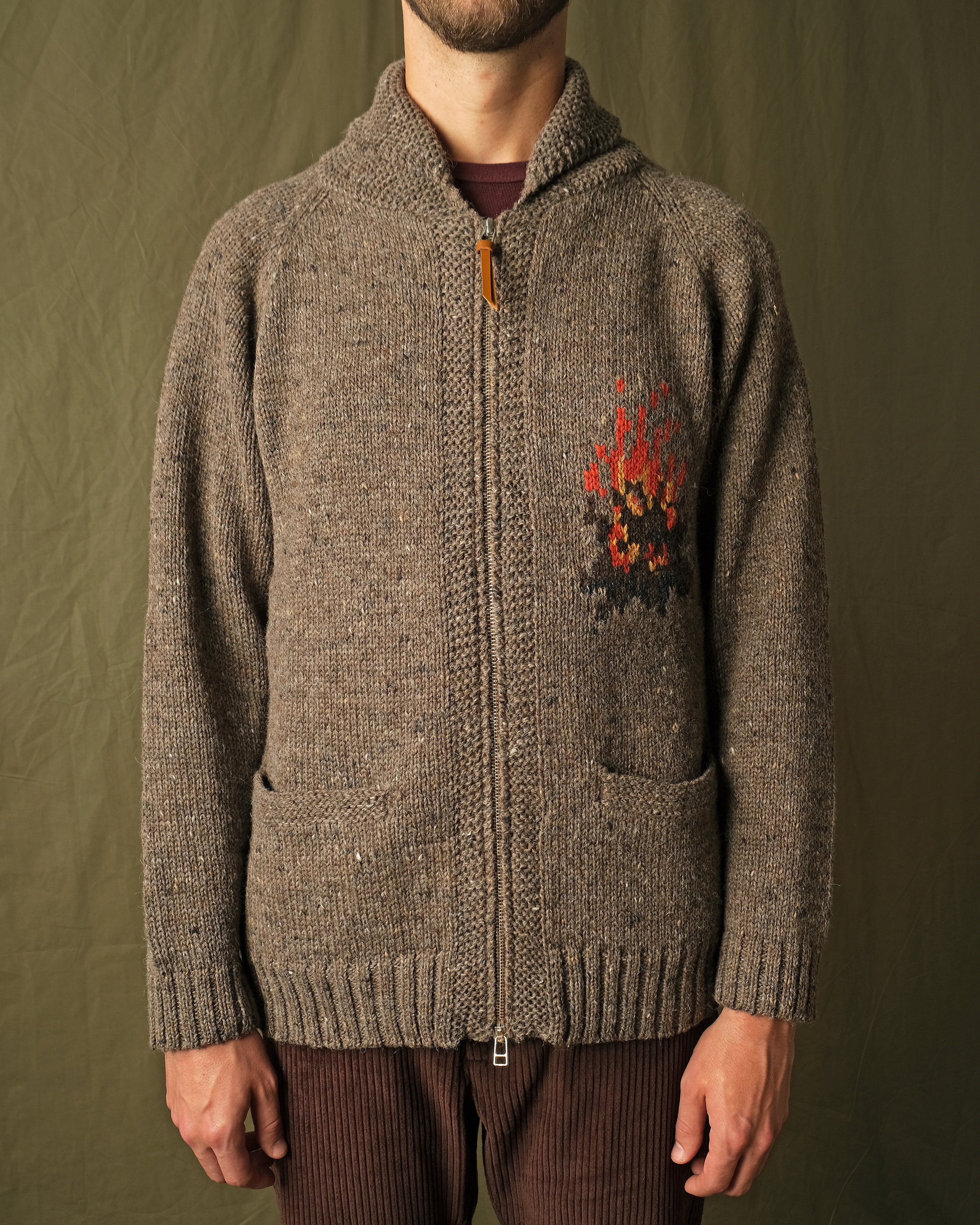 Brown full-zip cardigan worn by a man, campfire motif on the chest and ribbed hem