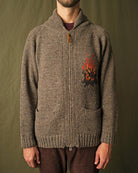 Brown full-zip cardigan worn by a man, campfire motif on the chest and ribbed hem