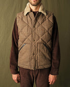 Brown diamond-quilted down vest with tan sherpa collar over ribbed knit sleeves