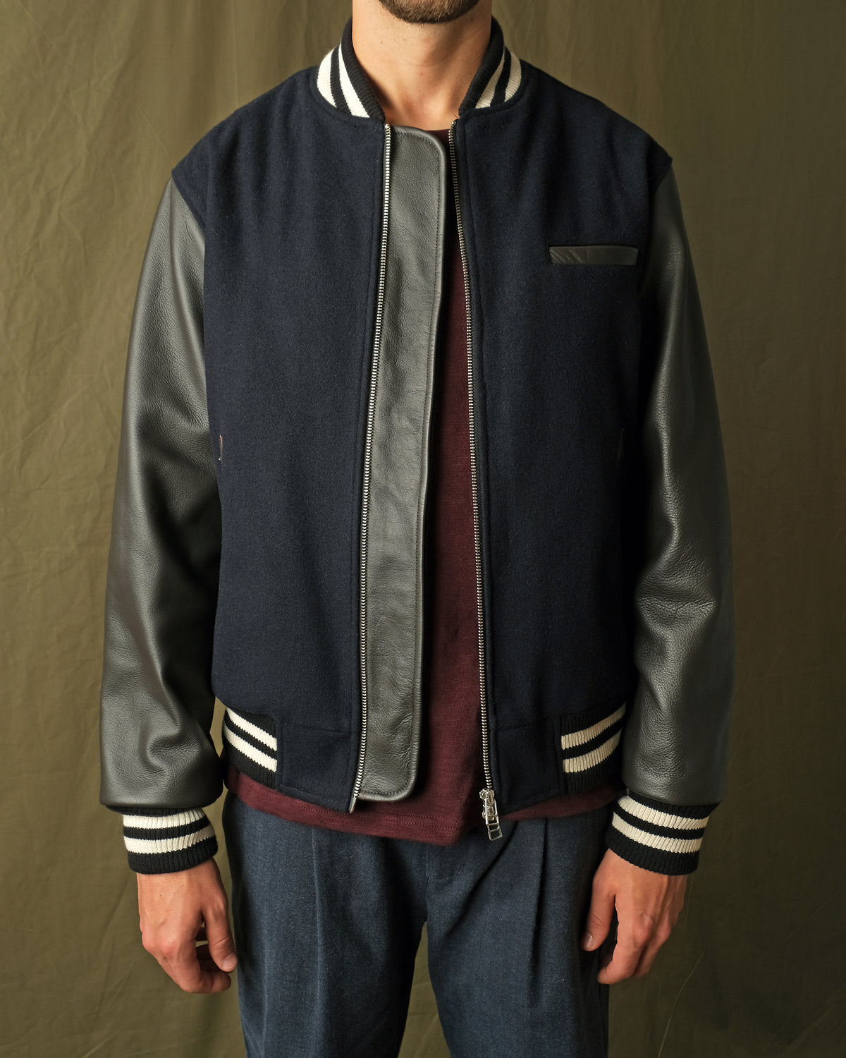 Navy bomber jacket with leather-look sleeves, striped cuffs, and front zipper