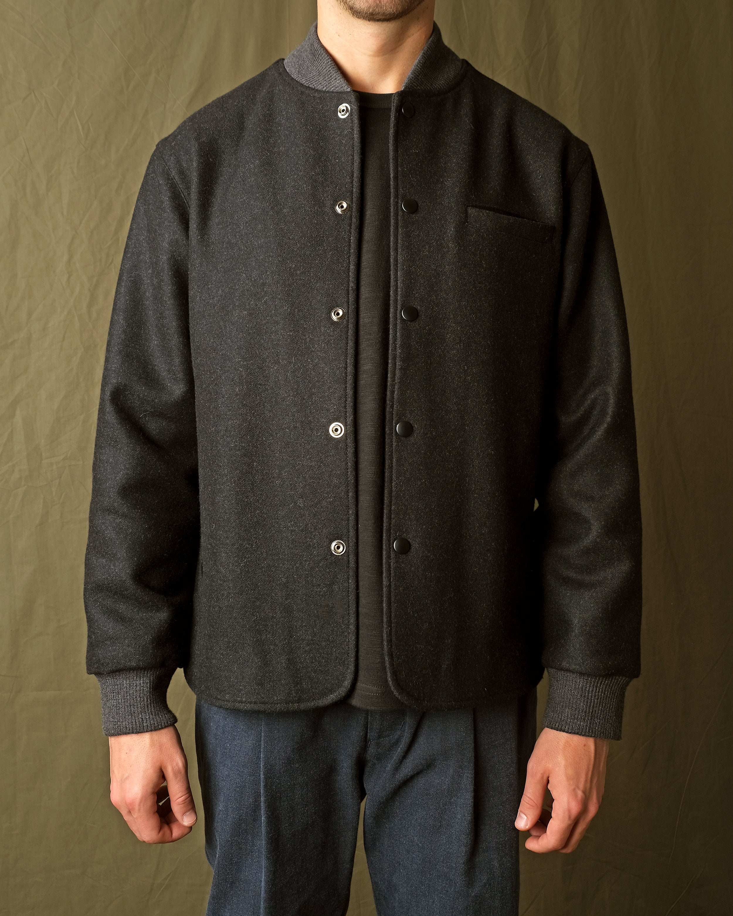 Charcoal stadium jacket front close-up with snap placket and ribbed cuffs
