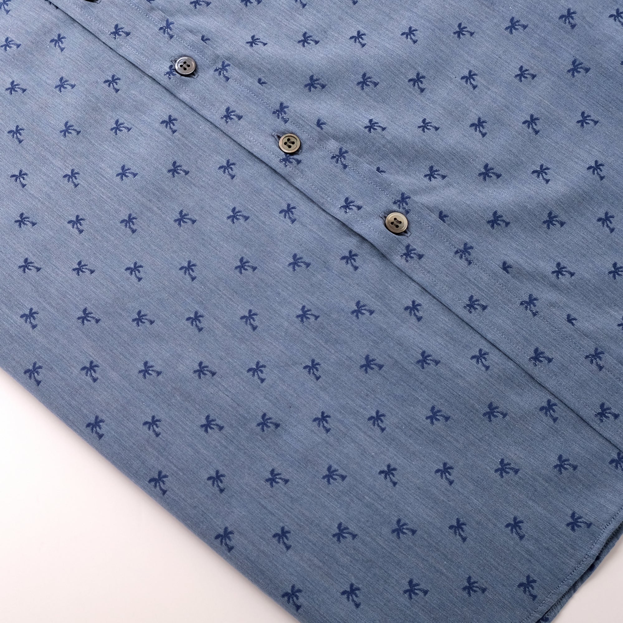 Light blue shirt placket with navy palm pattern and button closure